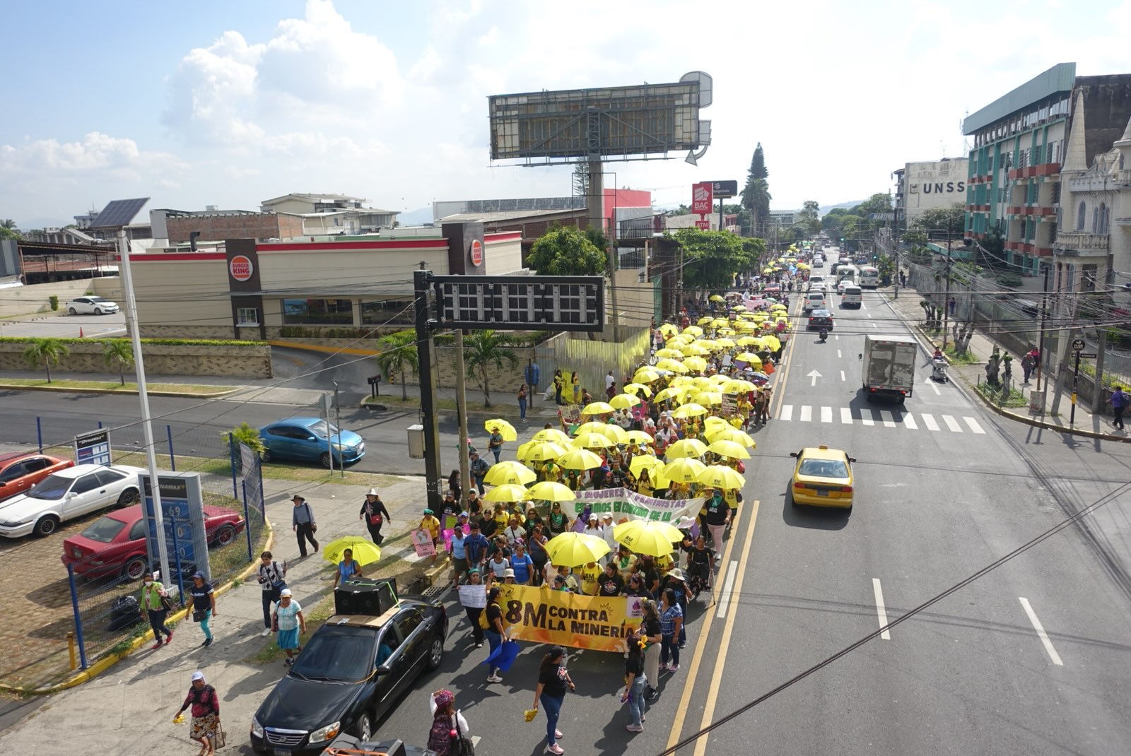 A crowd dressed in yellow marches with a banner that says "8m Against Mining"