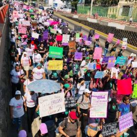 Image of hundreds of people marching in San Salvador, carrying signs denouncing patriarchal violence and other messages for International Women's Day