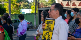 Man holding a yellow sign that says "Libertad para los lideres comunitarios" stands in a crowd