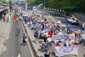 A crowd of people march down a wide street holding signs and banners