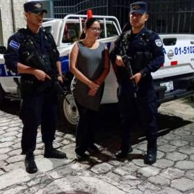 a woman in handcuffs stands between two police officers in blue uniforms in front of a police pick-up truck