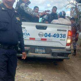 A policeman stand behind a police truck with two men in fatigues and two other men sitting in the bed