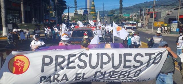 People, dressed in white, march with banner that says "Presupuesto para el Pueblo"