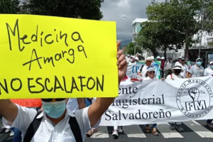 Man holds sign at march that reads, in Spanish, "Bitter medicine equals no pay scale" in front of a teachers union banner