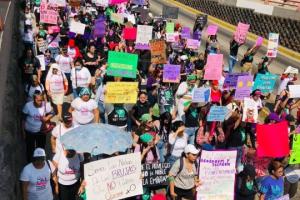 Image of hundreds of people marching in San Salvador, carrying signs denouncing patriarchal violence and other messages for International Women's Day