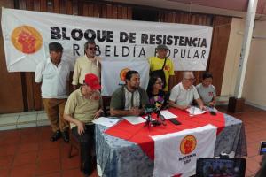 Leaders of the Popular Resistance and Rebellion Bloc sit at a table for a press conference in front of a banner