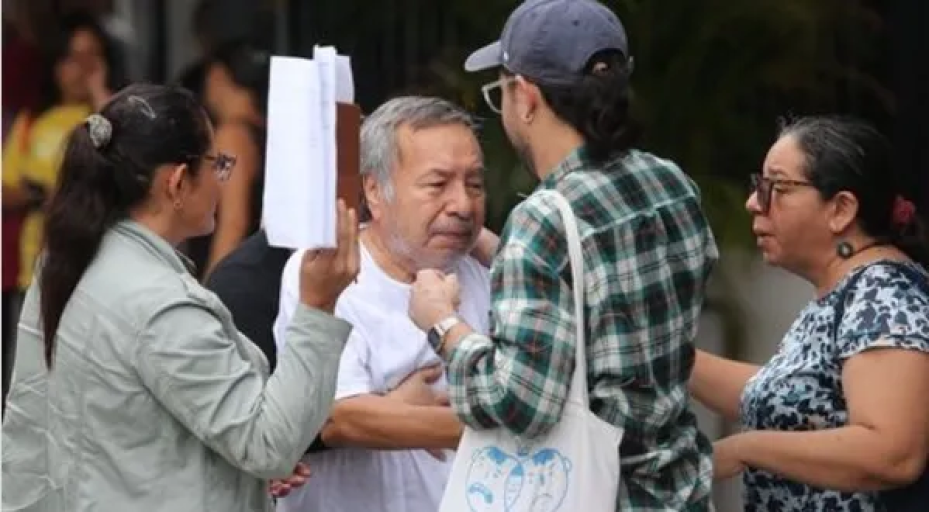 Atilio Montalvo, in a white t-shirt, reaches towards three family members to hug them