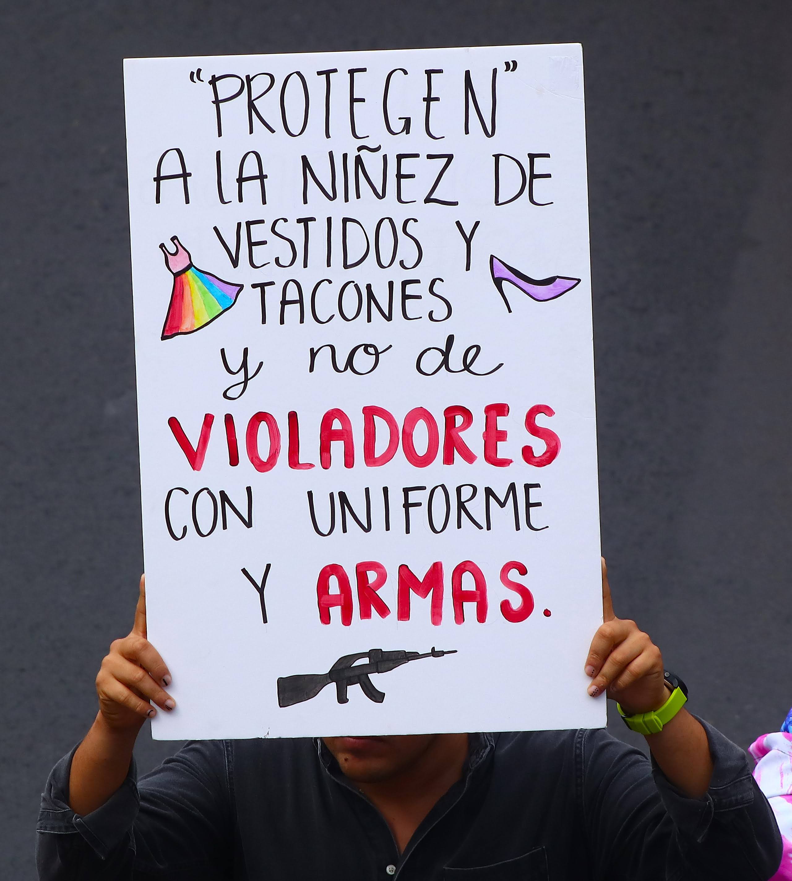 A protesers holds a sign that says "They 'protect' children from dresses and high heels, but not rapists with uniforms and guns"