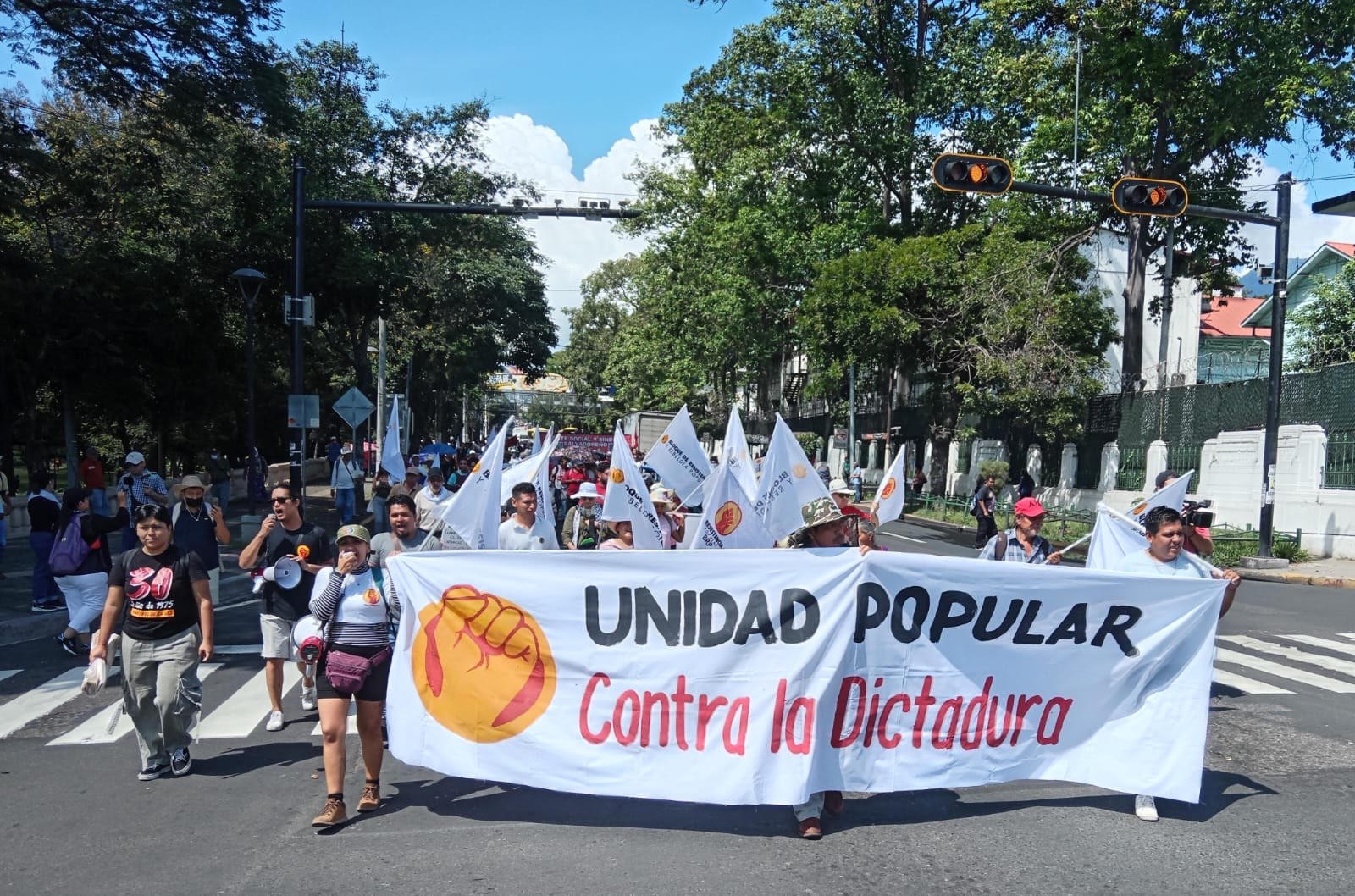 Protesters march with white banner with red letters that say "Unidad Popular Contra la Dictadura"